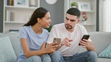 Güzel bir çift evde birlikte eğleniyor, kanepede oturuyor, rahat oturma odalarında akıllı telefonlarıyla mesajlaşırken rahatça gülümsüyorlar.
