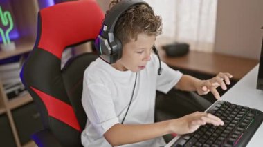 Sevimli sarışın çocuk muzaffer bir kutlama yapıyor, oyun meraklısı kazanıyor, karanlık bir oyun odasında gülümsüyor, dijital eğlenceye dalmış.