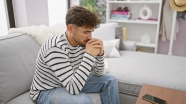Genç Arap adam, stresli ve yalnız, oturma odasındaki kanepesinde çaresizce oturuyor, depresyon ve endişe krizinin ortasında iç çatışma ve duygularla boğuşuyor.