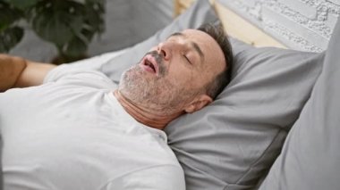 Orta yaşlı, kır saçlı, ciddi derecede hasta, sürekli öksürüyor, rahat yatak odasında sıcak bir battaniyenin altında uzanıyor, evinin içindeki griple savaşıyor.