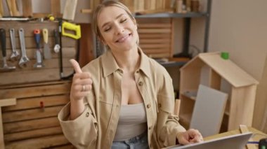 Genç sarışın kadın dizüstü bilgisayar kullanıyor mutlu ve pozitif gülümsüyor, başparmağını kaldırıyor ve marangozluğun onayını alıyor.