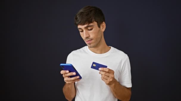 年轻自信的他的惊慌失措的男人乐于打字 喜欢用信用卡和智能手机在孤立的黑色背景下网上购物 — 图库视频影像