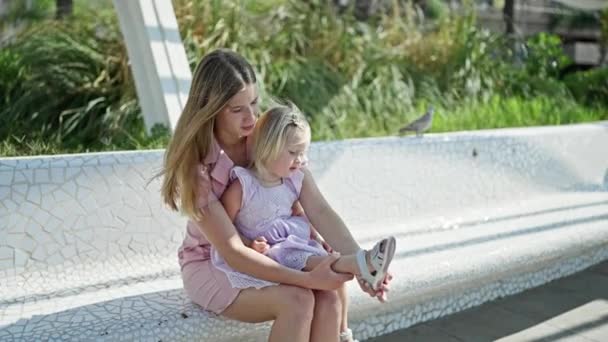 母と娘の瞬間 お母さんは公園のベンチに座って 緑豊かな自然の中で彼女の小さな女の子に靴を置く — ストック動画