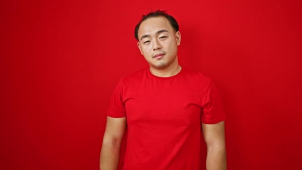 自信的中国年轻人站在红色的背景上 用一个 的手势把大拇指一闪一闪 他的微笑闪烁着幸福的光芒和淡淡的时尚 — 图库视频影像