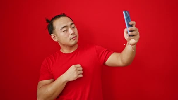 Молодой Китаец Улыбается Уверенно Делая Селфи Смартфоне Изолированном Красном Фоне — стоковое видео