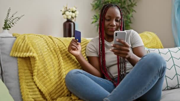 聪明而美丽的非洲女人一边坐在沙发上一边一边发短信 一边在网上购物 智能手机上还带着信用卡 — 图库视频影像