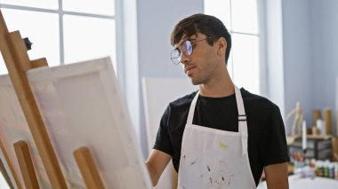 Yakışıklı genç İspanyol ressam, gerçekten konsantre olmuş, rahatlamış stüdyoda tuvale çizim yapıyor, üniversite sanat sınıfında fırça ve paletle yaratıcılığı öğreniyor..