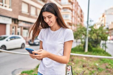 Genç, güzel, İspanyol bir kadın sokakta akıllı telefon kullanarak gülümsüyor.