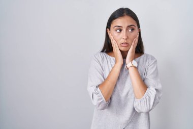 Beyaz arka planda duran genç İspanyol kadın yorgun eller yüzünü, depresyonu ve üzüntüyü örten, sorun yüzünden üzgün ve sinirli. 