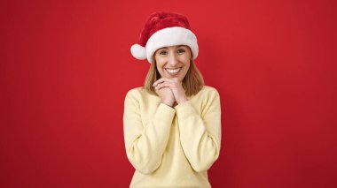 Genç sarışın, kendine güvenen, kırmızı arka planda Noel şapkası takan bir kadın.