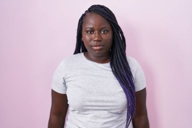 Pembe arka planda duran genç Afrikalı kadın yüzünde ciddi bir ifadeyle rahatlamış. Basit ve doğal bir şekilde kameraya bakıyorsun.. 