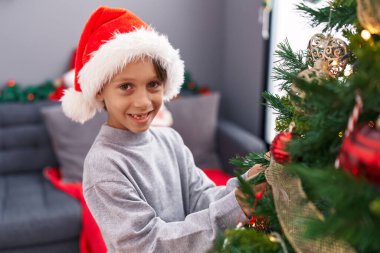 Tapılası İspanyol çocuk gülümseyerek evde kendine güvenen bir Noel ağacı süslüyordu.