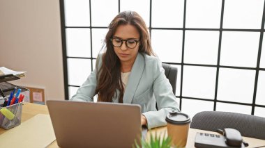 Ciddi ama rahat, odaklanmış genç bir İspanyol kadın zarif bir patron rolünü üstlenir. Güzel bir profesyonel. Ofis masasında dizüstü bilgisayarıyla özenle çalışıyor..