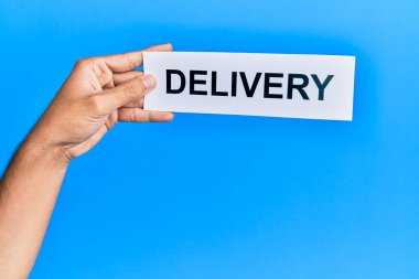 Hand of caucasian man holding paper with delivery word over isolated blue background