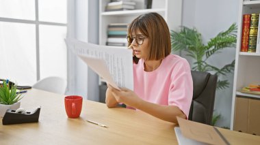 Güzel bir İspanyol kadın işçi, ofis masasında evrak okurken akıllı telefondan iş konuşmaya odaklanmış.