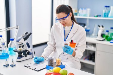 Young beautiful hispanic woman scientist weighing food writing report at street