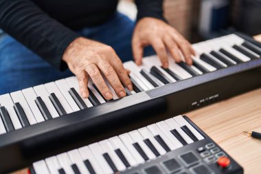Middle age grey-haired man musician playing piano at music studio