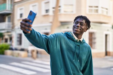 Afro-Amerikalı adam gülümsüyor. Kendine güveni tam. Sokakta akıllı telefondan selfie çekiyor.