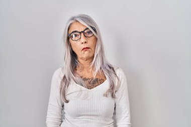 Beyaz arka planda duran gri saçlı orta yaşlı kadın uykulu ve yorgun görünüyor, yorgunluktan yorgun ve akşamdan kalma, sabahları tembel gözler.. 