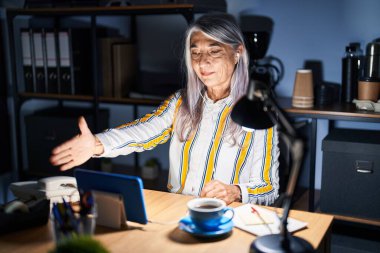 Gri saçlı, gece ofiste çalışan orta yaşlı bir kadın selamlaşma ve dostça bir şekilde tokalaşmak için gülümsüyor. başarılı iş. 