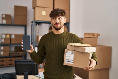 Sakallı bir Arap, küçük bir şirkette çalışıyor teslimat paketlerini tutuyor, gülümsüyor ve başka tarafa bakıyor.. 