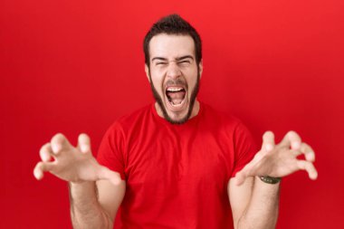 Gündelik kırmızı tişört giyen genç İspanyol adam komik bir şekilde gülümsüyor kedi gibi pençe hareketi yapıyor, agresif ve seksi bir ifade. 
