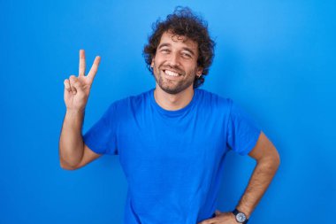 Mavi arka planda dikilmiş gülümseyen İspanyol genç adam parmaklarını zafer işareti yaparken kameraya bakıyor. İki numara.. 