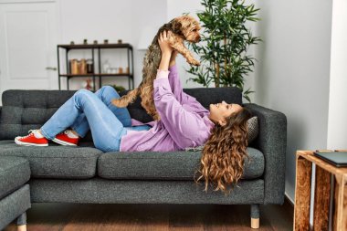 Genç, güzel, İspanyol bir kadın evdeki kanepede köpeğe sarılıyor.