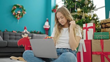 Genç sarışın kadın evde dizüstü bilgisayar kullanarak Noel 'i kutluyor.