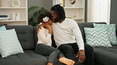 Afro-Amerikan baba ve kızı gülümsüyor. Birbirlerine sarılıyorlar. Kanepede oturmuş, evlerinde öpüşüyorlar.