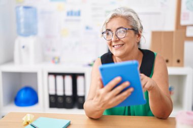 Ofiste dokunmatik ped kullanan, orta yaşlı, kır saçlı iş kadını.