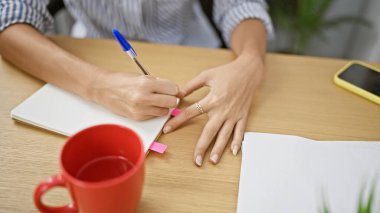 Başarılı İspanyol iş kadını, ofis masasında gevşemiş, elleri iş başarısı için iş notları almakla meşgul kahve içerken