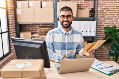 Genç bir İspanyol iş adamı ofiste dizüstü bilgisayarla paket tutuyor.