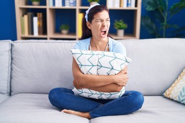 Kanepede oturan Latin asıllı genç kadın kızgın ve kızgın bağırıyor öfkeyle bağırıyor. öfke ve agresif konsept. 