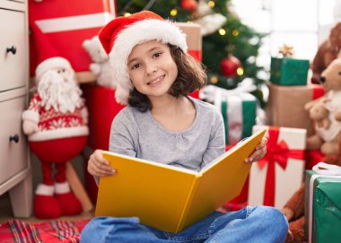 Evdeki Noel ağacının yanında oturmuş kitap okuyan sevimli Çinli kız.