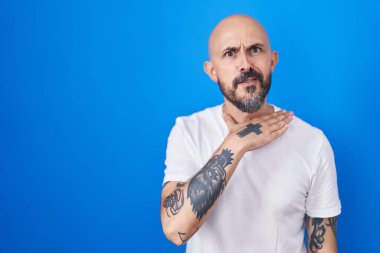 Mavi arka planda dikilen İspanyol dövmeli adam bıçak niyetine boğazını kesiyor, saldırganlığı şiddetle tehdit ediyor. 