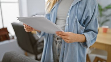 Çekici sarışın kadın işçi yoğun bir şekilde iş belgesi okuyor, ofiste duruyor, patron enerjisi saçıyor.