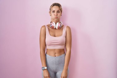 Spor giyinen, kulaklık takan, komik yüzlü genç sarışın kadın. Havayla şişmiş ağız, çılgın bir ifade.. 