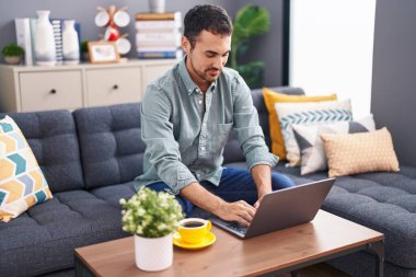 Genç İspanyol adam dizüstü bilgisayar kullanıyor ve evde kahve içiyor.