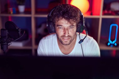 Genç İspanyol asıllı adam müzik stüdyosunda bilgisayar kullanarak video oyunu oynuyor.