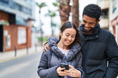 Man and woman couple smiling confident using smartphone at street