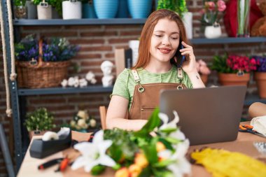 Çiçekçide bilgisayarla konuşan kızıl saçlı genç bir çiçekçi.