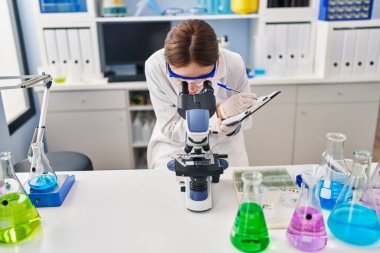 Genç sarışın bilim adamı laboratuardaki belgelerde mikroskop kullanıyor.