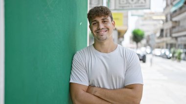 Neşeli, genç İspanyol bir adam canlı bir şehir caddesinde dururken kendine güveni yayıyor. Kollarını kavuşturup, pozitiflik ve çekicilik gösterisi yapıyor..