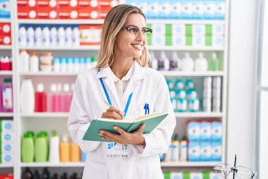 Young blonde woman pharmacist writing on document at pharmacy