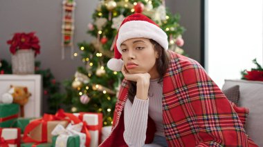 Genç, güzel, İspanyol bir kadın Noel ağacının yanında, koltukta oturmuş, üzgün üzgün üzgün eve bakıyor.
