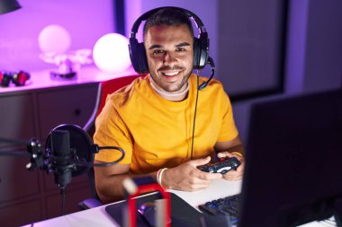 Young hispanic man streamer playing video game using joystick at gaming room