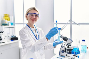 Genç sarışın bilim adamı laboratuarda test tüplerini inceliyor.