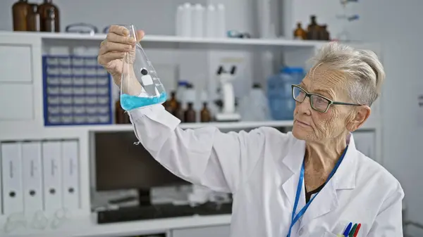 屋内実験室のテスト管の灰色髪の女性の科学者働き 測定の液体は医学研究の安全そして精密を細心に保障します — ストック写真
