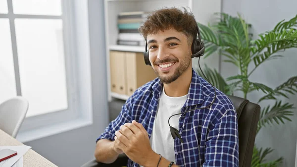 Happy arab man with confident smile, working in business, graces his office space, bossing about wearing headset to aid customer service